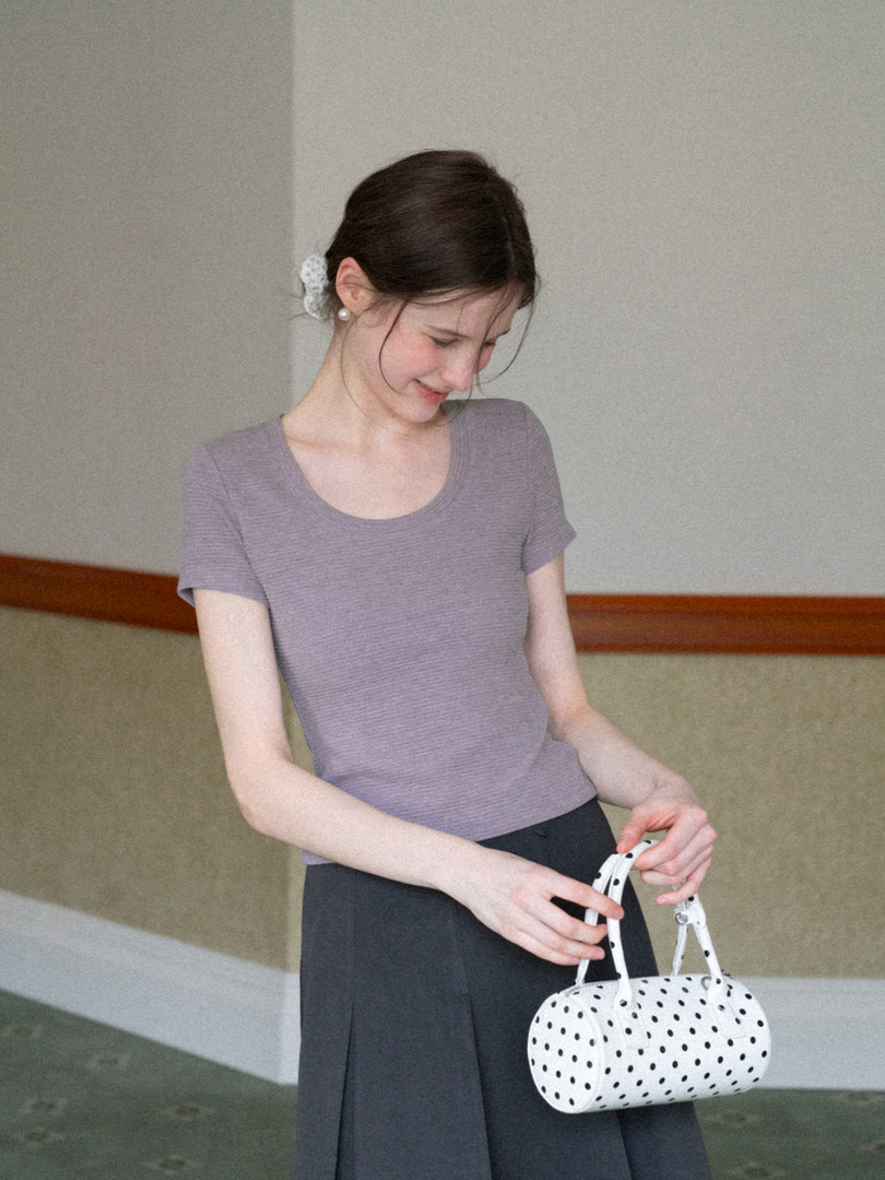 Woman wearing a lavender short-sleeve knit top and holding a white polka dot handbag