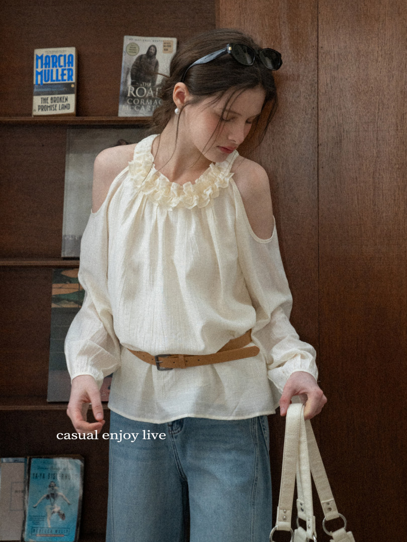 Woman wearing a cream ruffled cold-shoulder blouse with long sleeves