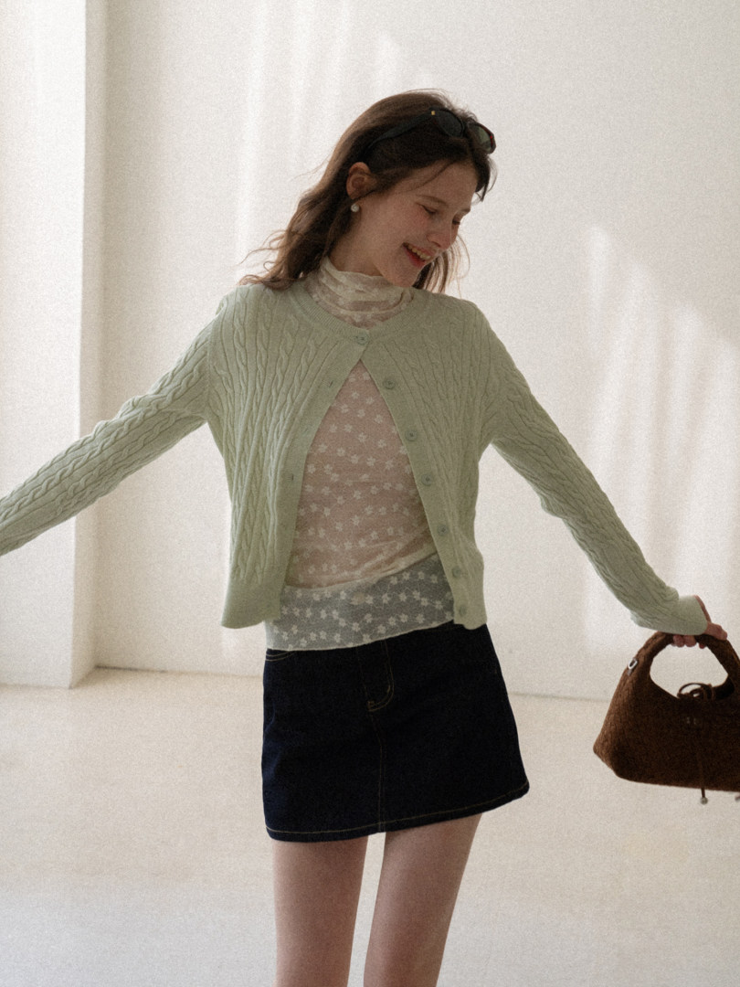 Light green cable-knit cardigan worn over a floral top with a dark denim skirt