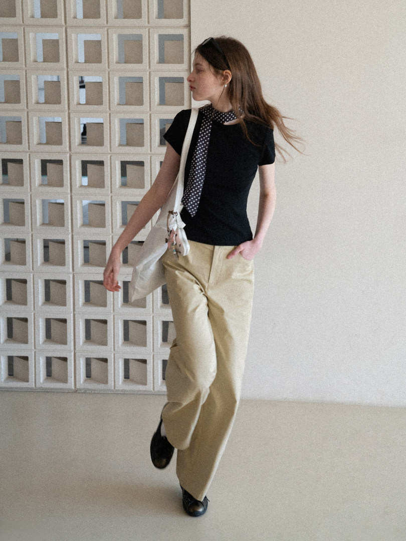 Model wearing a black top with beige trousers, a polka dot scarf, and a white shoulder bag