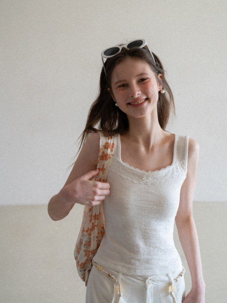 Woman wearing a white lace-trim tank top and light pants with a floral scarf bag
