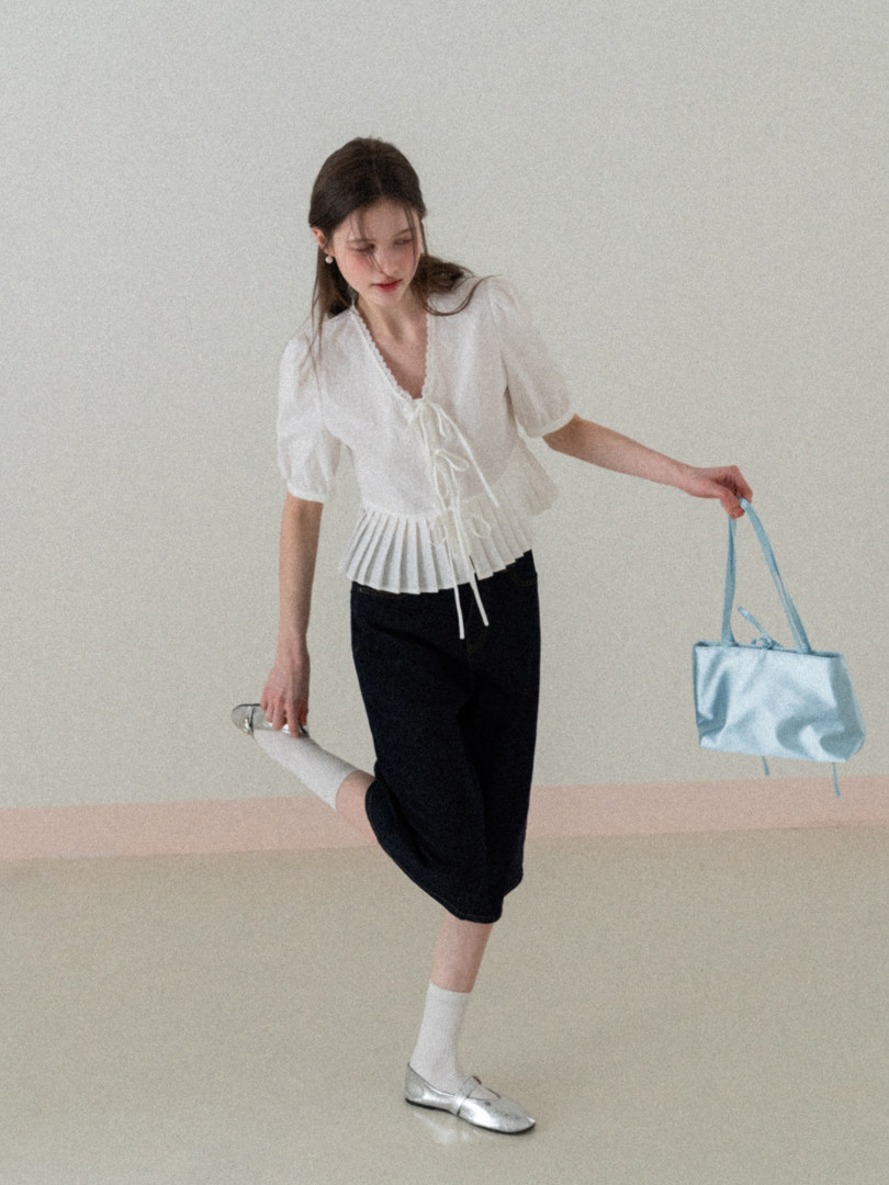 Woman wearing a white pleated tie-front blouse with black pants, silver flats, and a light blue tote bag