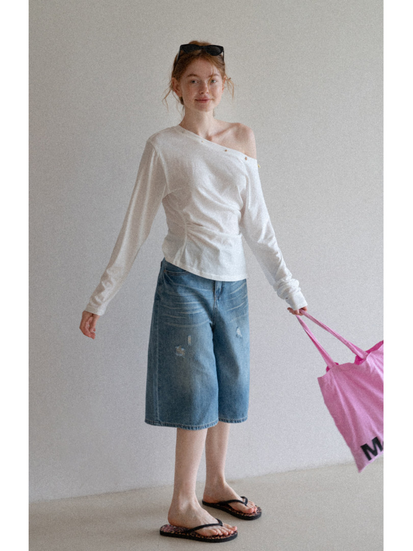 Model wearing a white off-shoulder long-sleeve top with denim shorts
