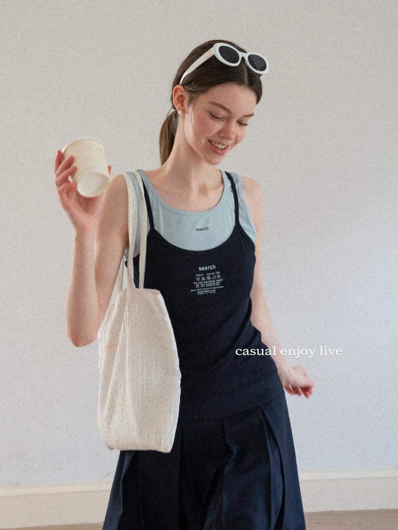 Woman wearing a black and light blue tank top with a navy skirt and canvas tote bag
