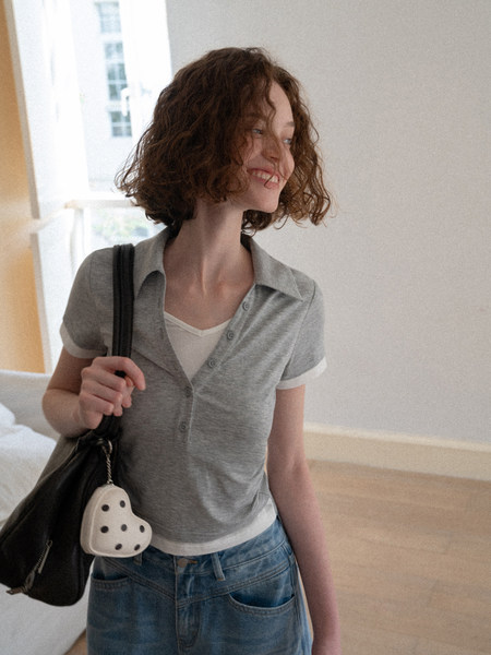 Woman wearing a gray short-sleeve button-up top over a white tank top with jeans