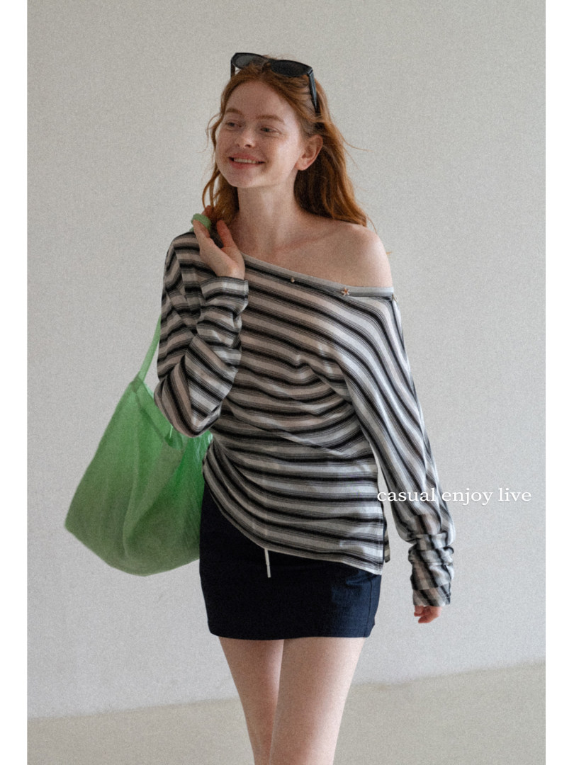 Model wearing a striped off-shoulder long-sleeve top with a dark mini skirt and green tote bag