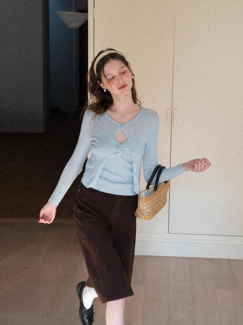 Woman wearing a light blue cardigan and top with dark cropped pants and a woven handbag