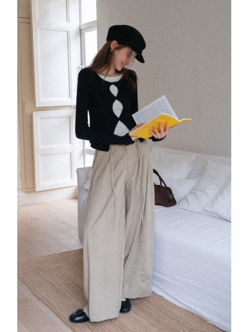Woman wearing a black top with beige wide-leg trousers and a black beret indoors