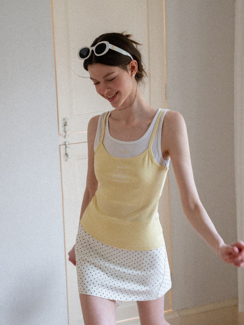 Woman wearing a yellow tank top layered over a white top with a polka dot mini skirt