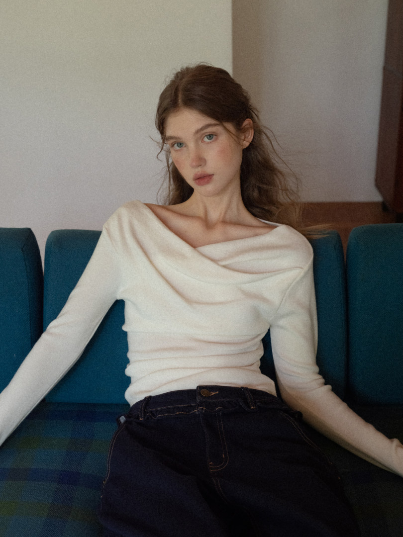 Woman wearing an off-white draped long-sleeve top with dark jeans