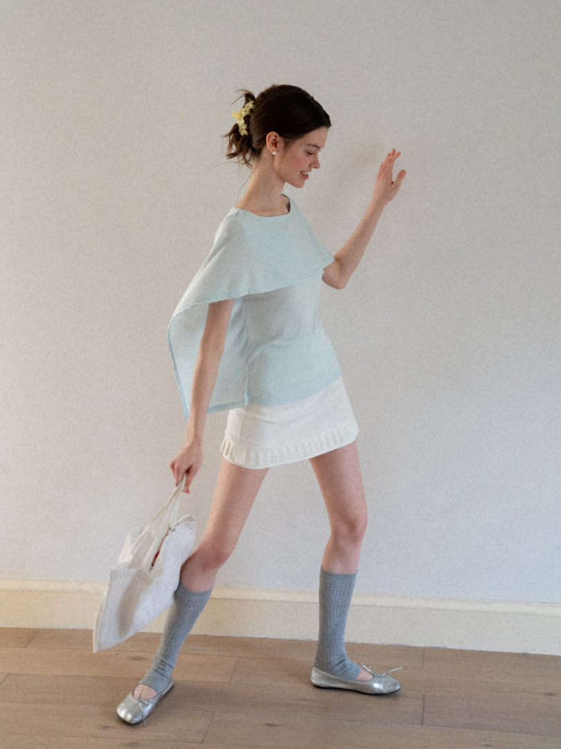 Model wearing a light blue top with a white mini skirt, gray socks, silver flats, and carrying a white bag
