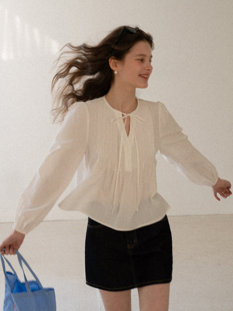 Woman wearing a white sheer tie-neck blouse with a black mini skirt