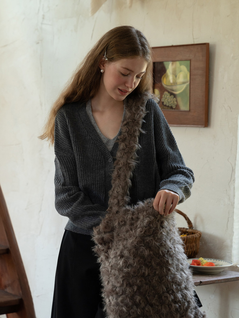 Model wearing a dark knit cardigan with a fluffy crossbody bag