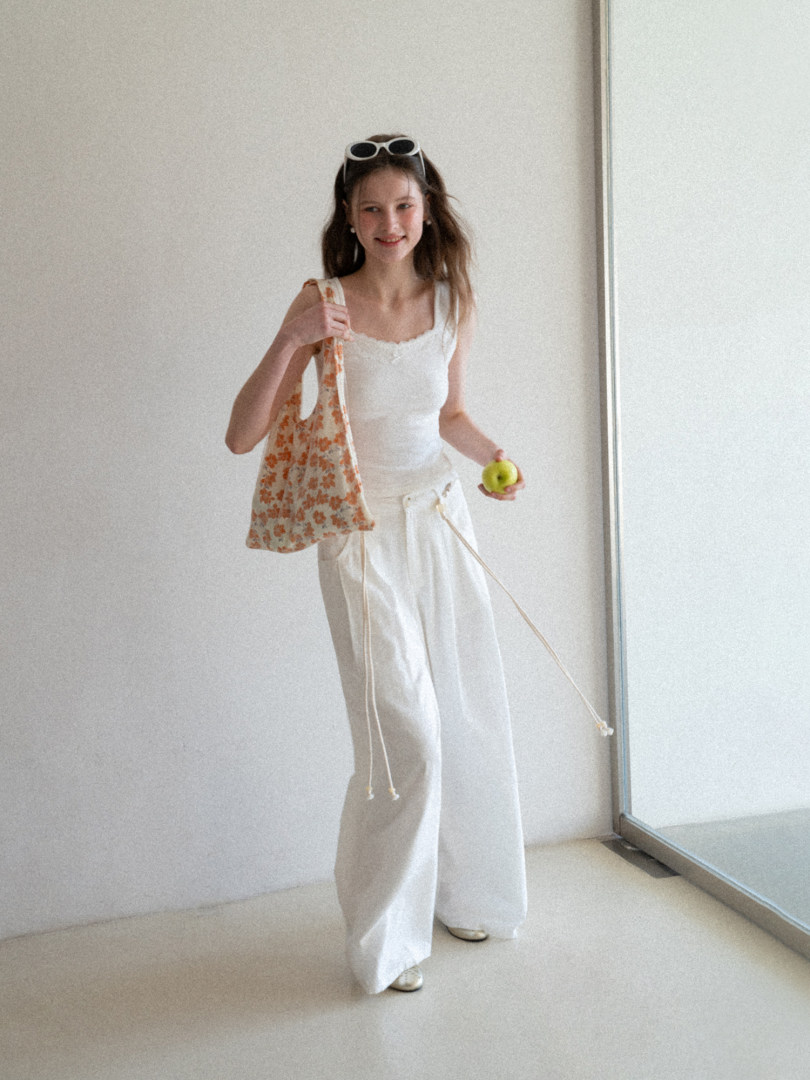 Woman wearing a white sleeveless top and wide-leg pants with a floral tote bag