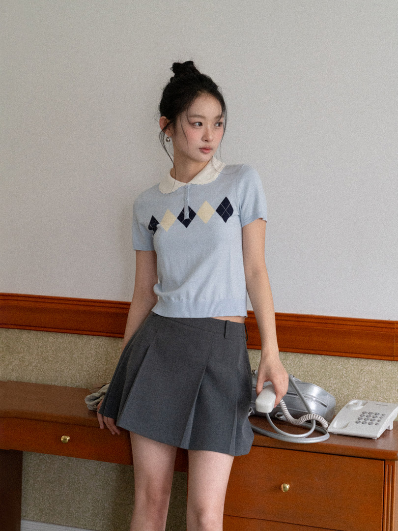 Model wearing a light blue short-sleeve argyle knit top with a dark pleated skirt