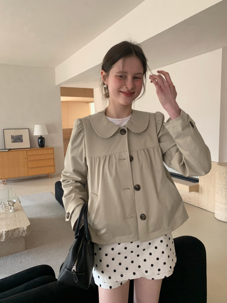 Woman wearing a beige button-up jacket with a polka dot skirt indoors