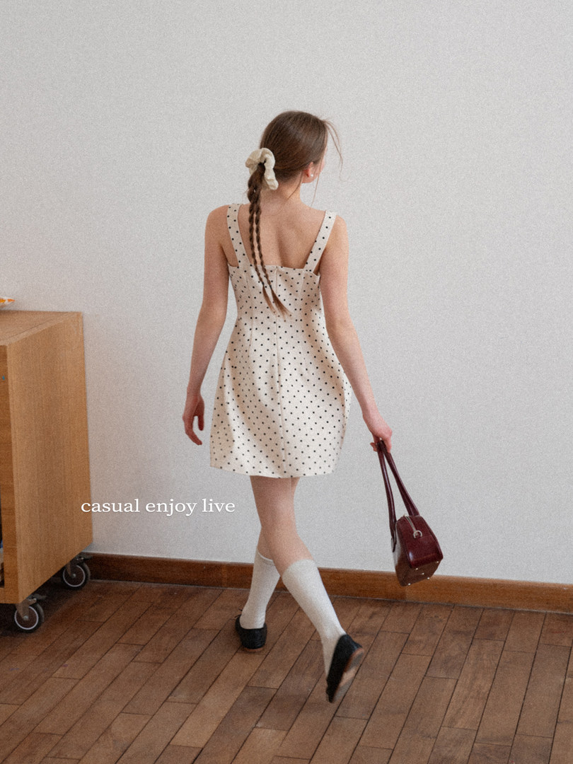 Model wearing a cream polka dot sleeveless mini dress with a handbag