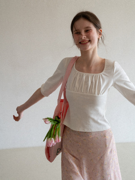 Woman wearing a white puff-sleeve blouse with a pink floral skirt and tote bag