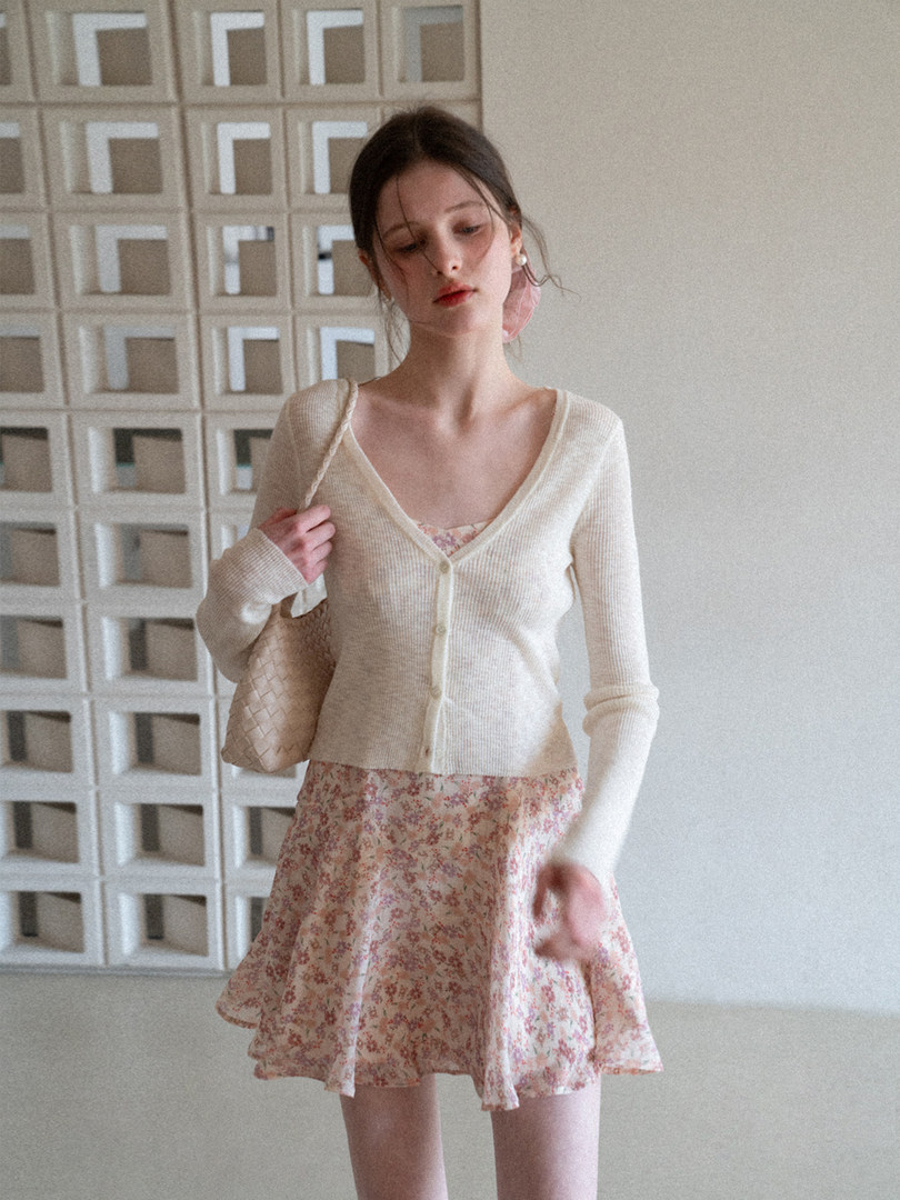 Model wearing a cream cardigan over a floral mini dress with a woven shoulder bag