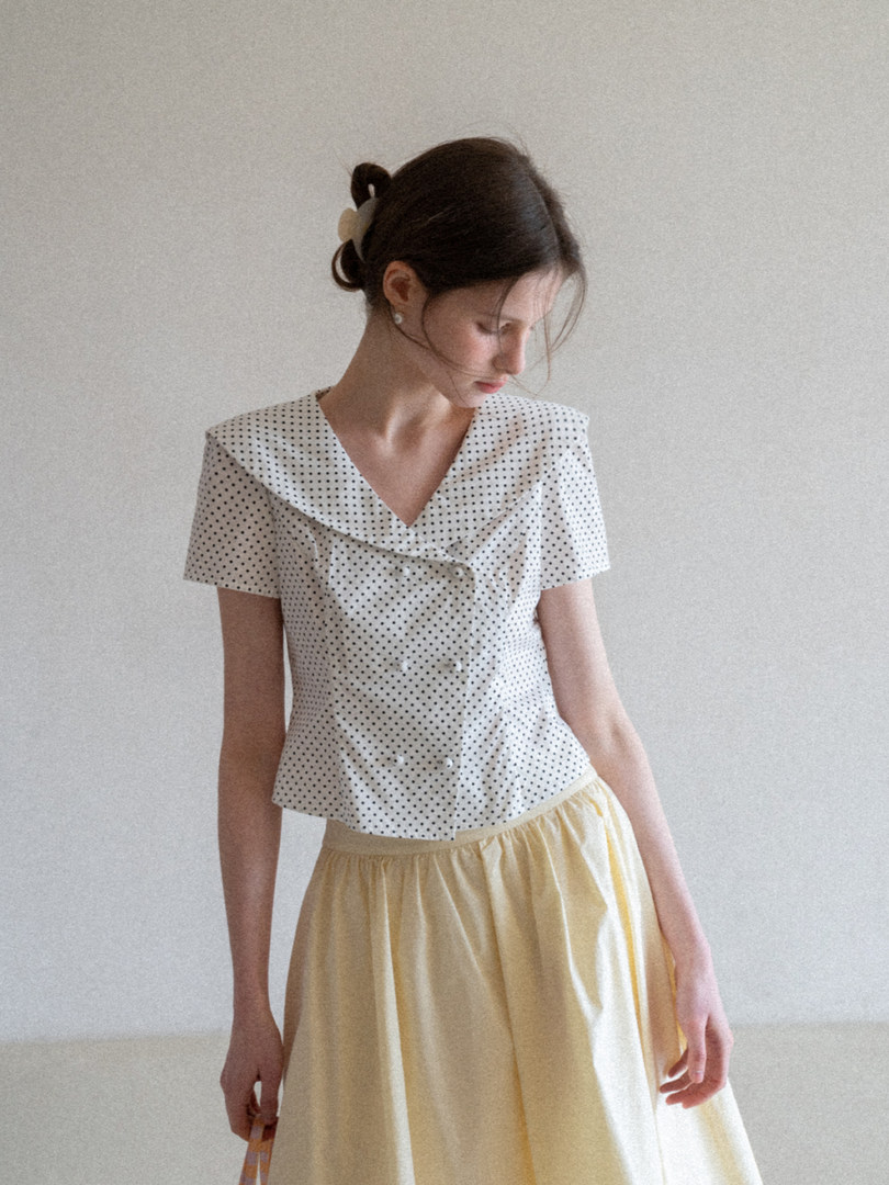 Woman modeling a white polka dot short-sleeve top with a light yellow skirt