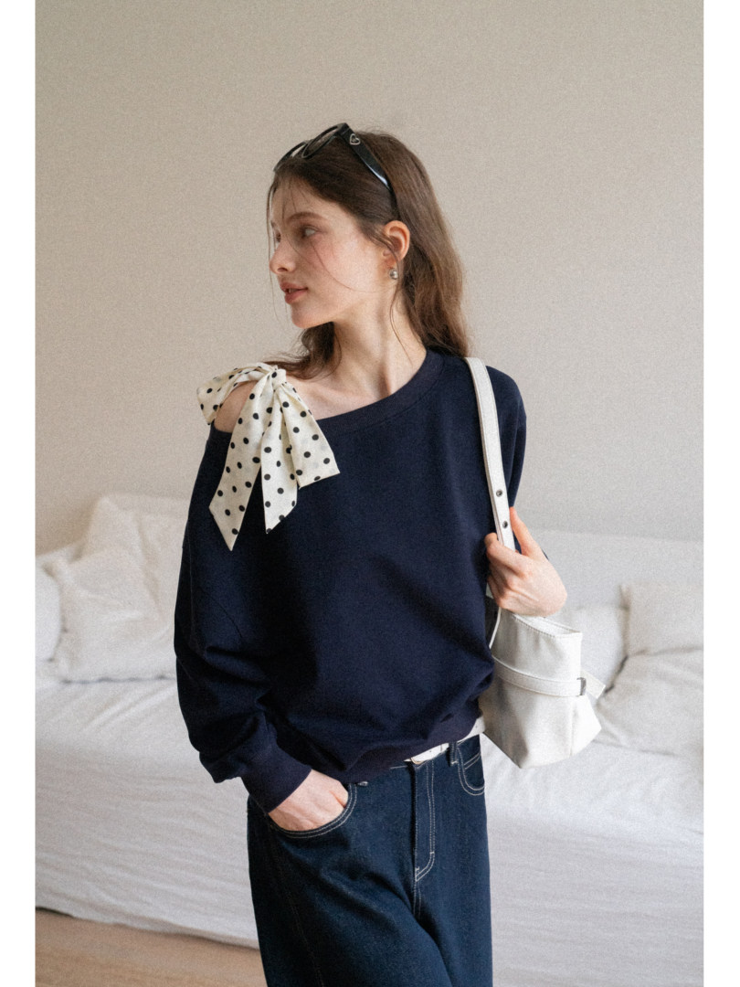 Woman wearing a navy off-shoulder sweater with a polka dot bow and a white shoulder bag