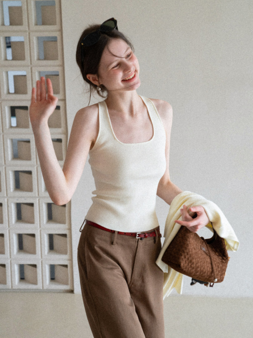 Woman wearing a cream ribbed tank top with brown trousers and a woven handbag