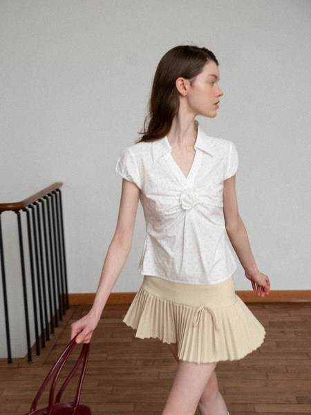 Model wearing a white short-sleeve blouse and beige pleated mini skirt