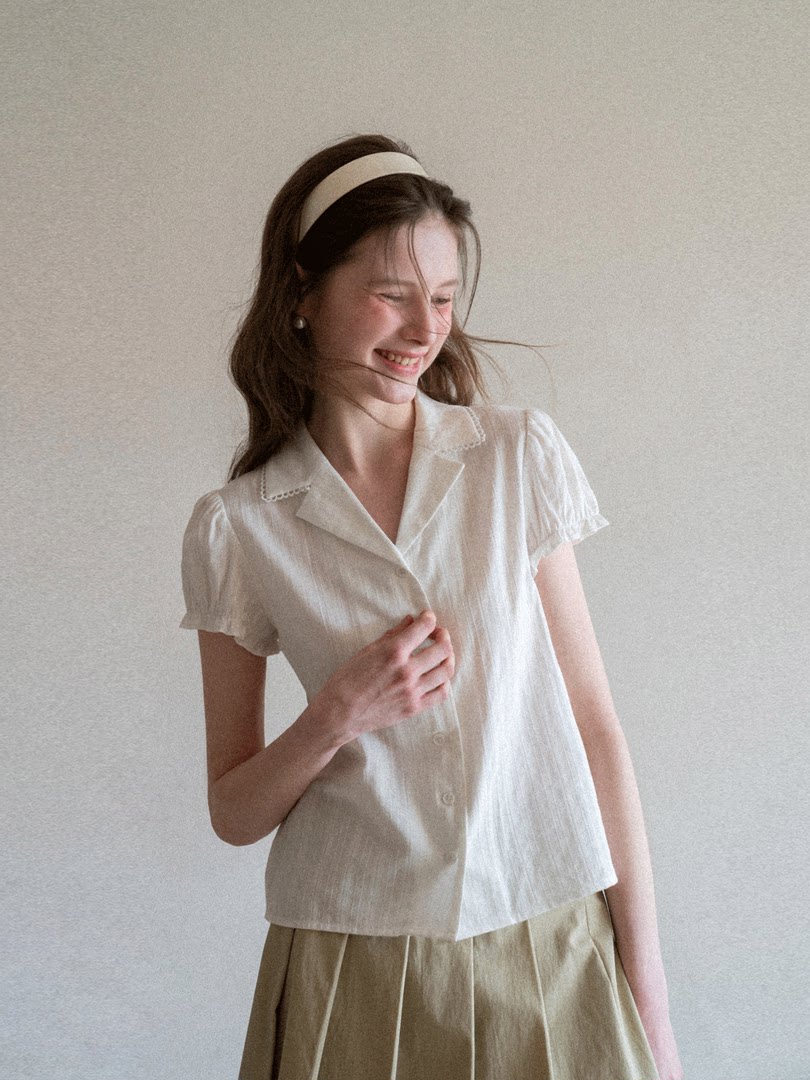Woman wearing a cream short-sleeve button-up blouse with a pleated skirt