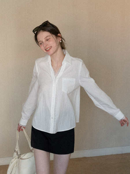 Model wearing a white button-up blouse with a black mini skirt and cream handbag