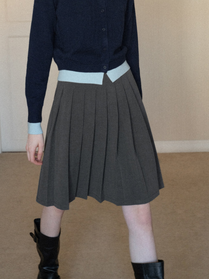 Model wearing a navy cardigan with a pleated gray skirt and black boots