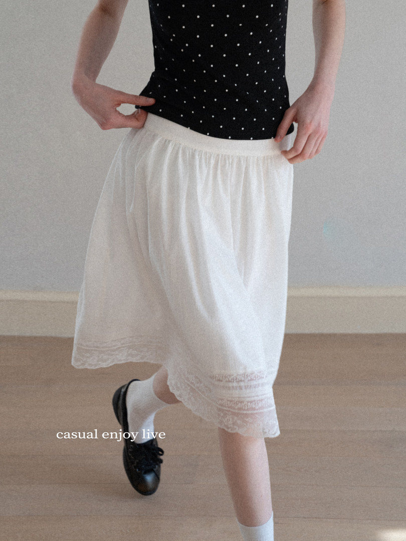 Woman wearing a white midi skirt with lace trim and a black polka dot top