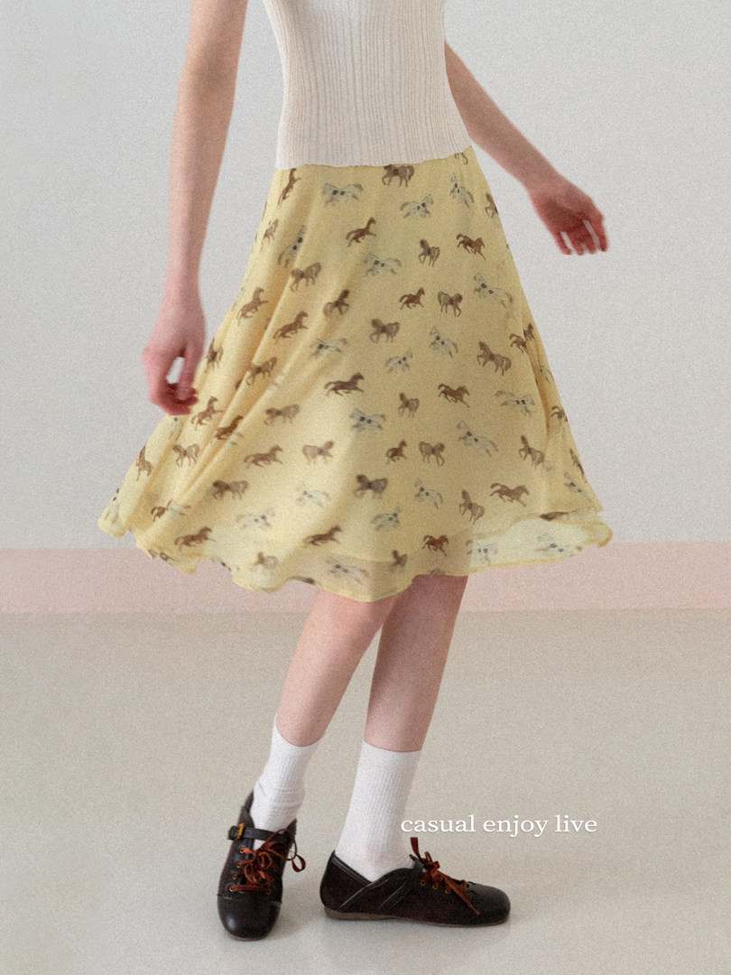 Model wearing a yellow printed flared skirt with a white knit top and black shoes