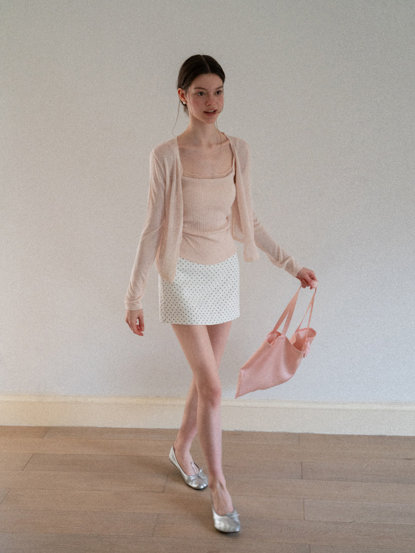 Model wearing a light beige cardigan, tank top, patterned mini skirt, and silver flats while holding a pink tote bag