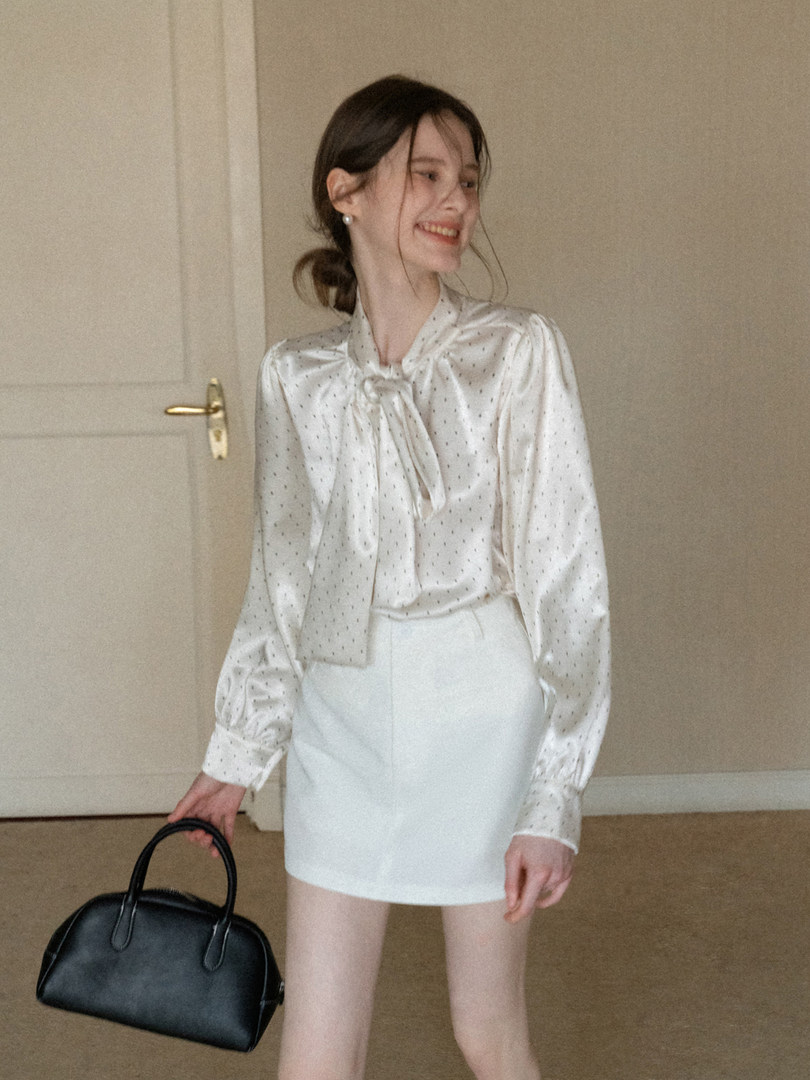 Woman modeling a satin blouse, white mini skirt, and black handbag