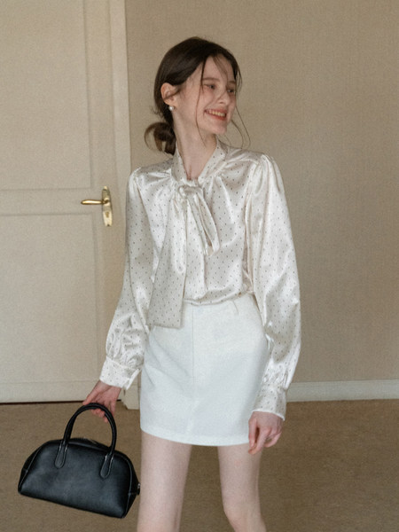 Woman modeling a satin blouse, white mini skirt, and black handbag