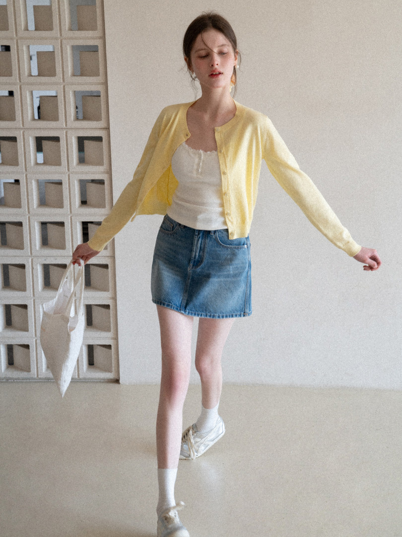 Model wearing a yellow cardigan over a white top with a denim mini skirt