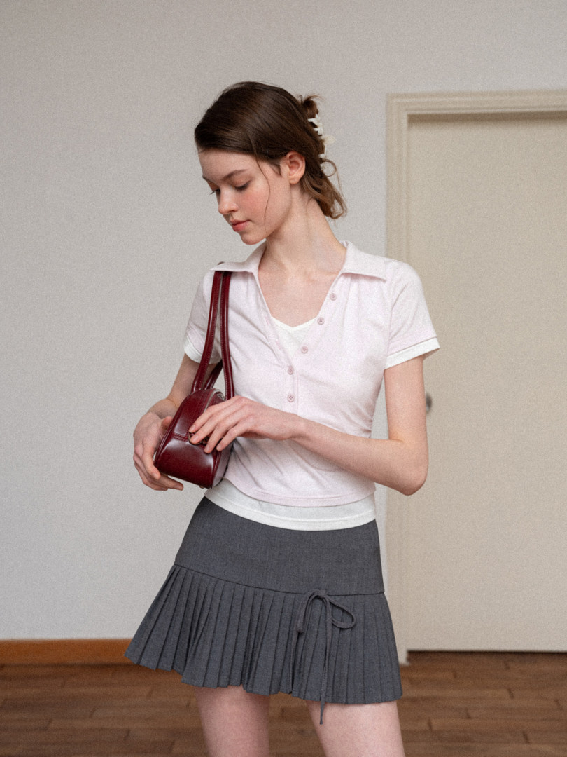 Woman wearing a white short-sleeve collared top and gray pleated skirt with a burgundy shoulder bag