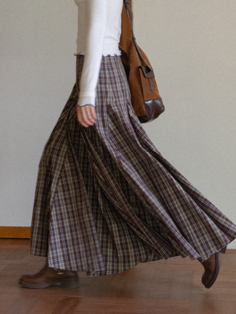 Model wearing a plaid maxi skirt with a light sweater and brown shoulder bag