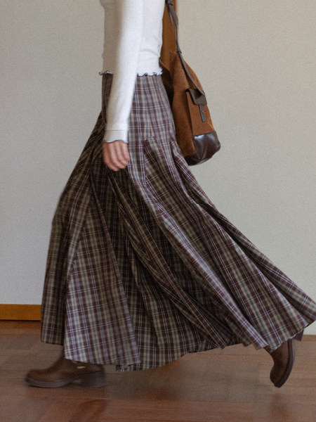 Model wearing a plaid maxi skirt with a light sweater and brown shoulder bag