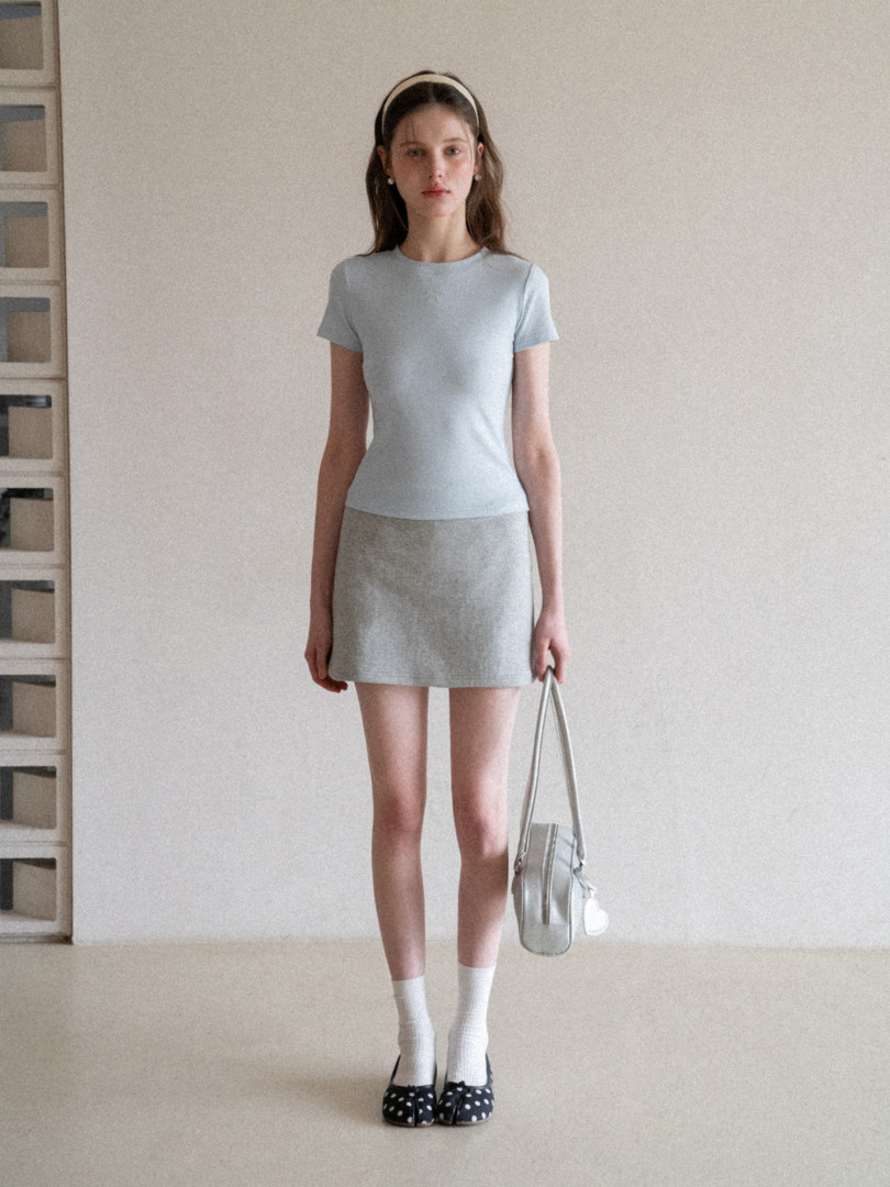 Model wearing a light blue fitted top with a gray mini skirt and handbag
