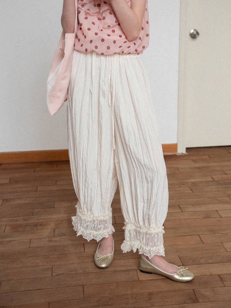Model wearing a pink polka dot top with cream lace-trimmed pants and gold flats
