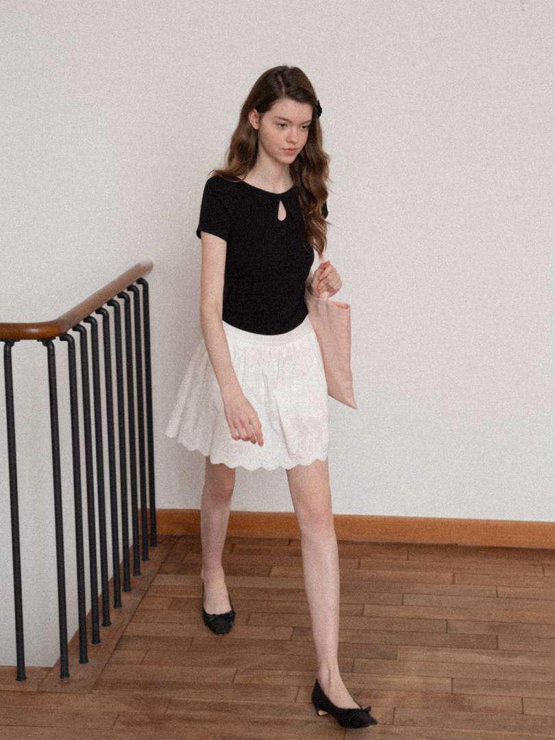 Woman wearing a black short-sleeve top with a white skirt and black flats