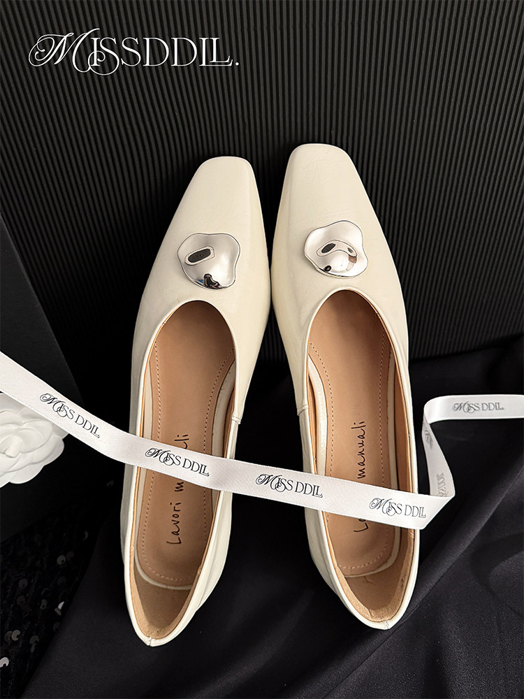Cream pointed-toe flats with metallic embellishments on a black background