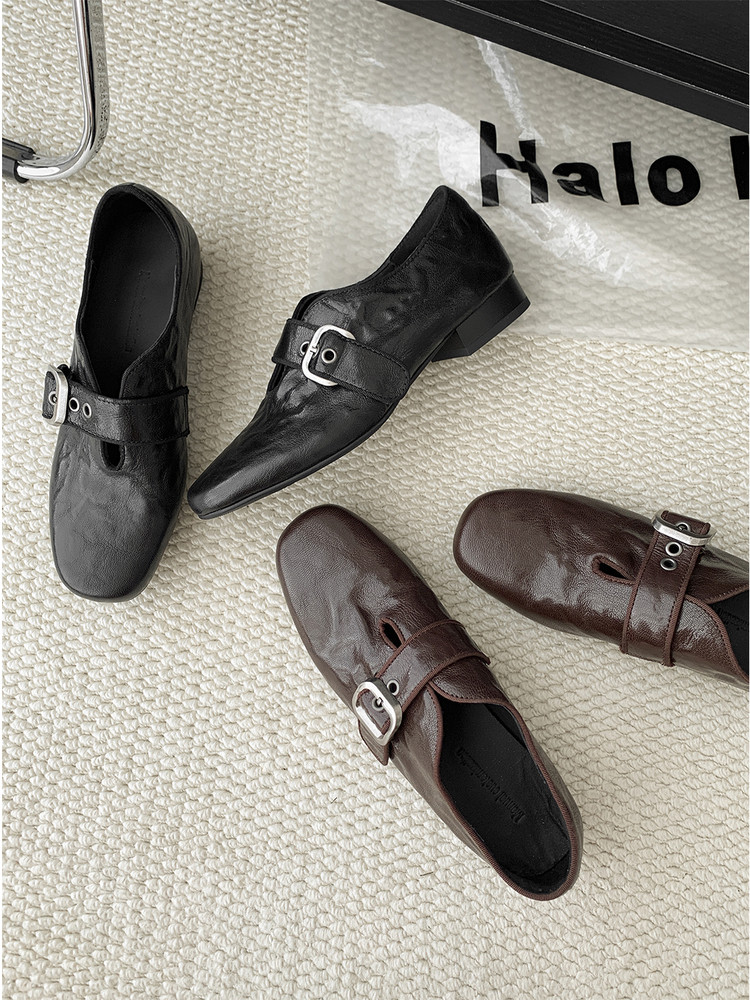 Black and brown leather buckle shoes displayed on a textured surface