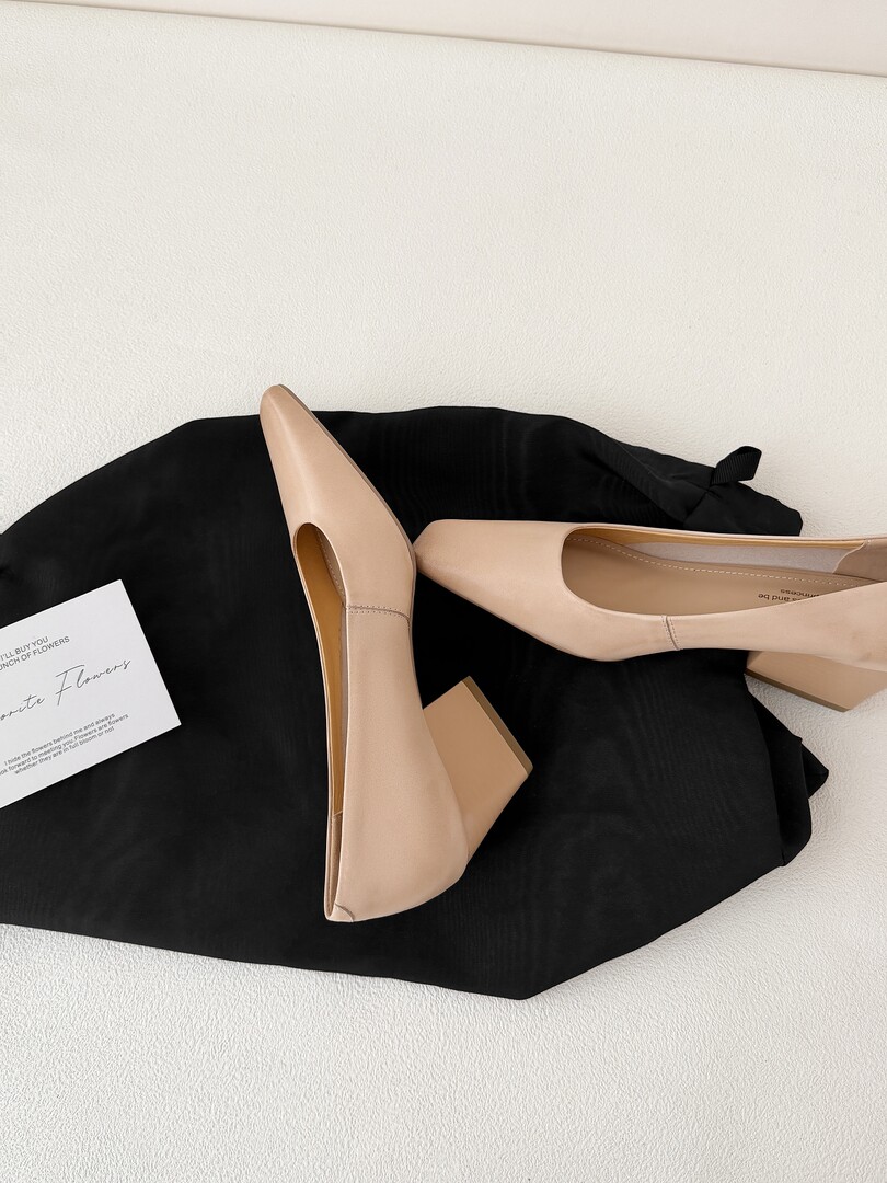 Beige pointed-toe high-heel pumps on a black fabric backdrop