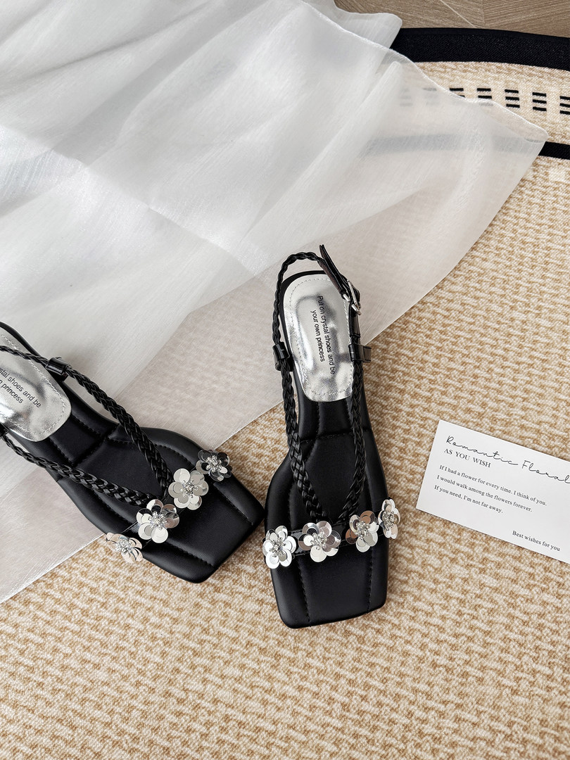 Black floral-embellished strappy sandals laid flat on a textured surface