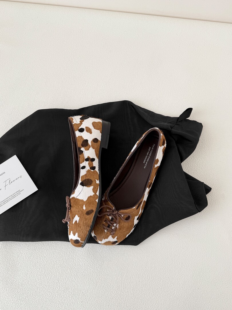 Pair of cow-print flat shoes displayed on a black garment