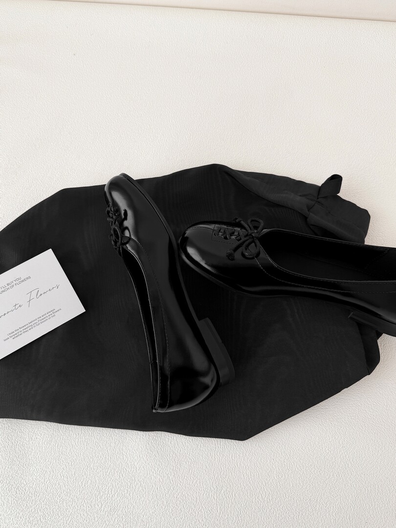 Black glossy lace-up dress shoes displayed on a black cloth background