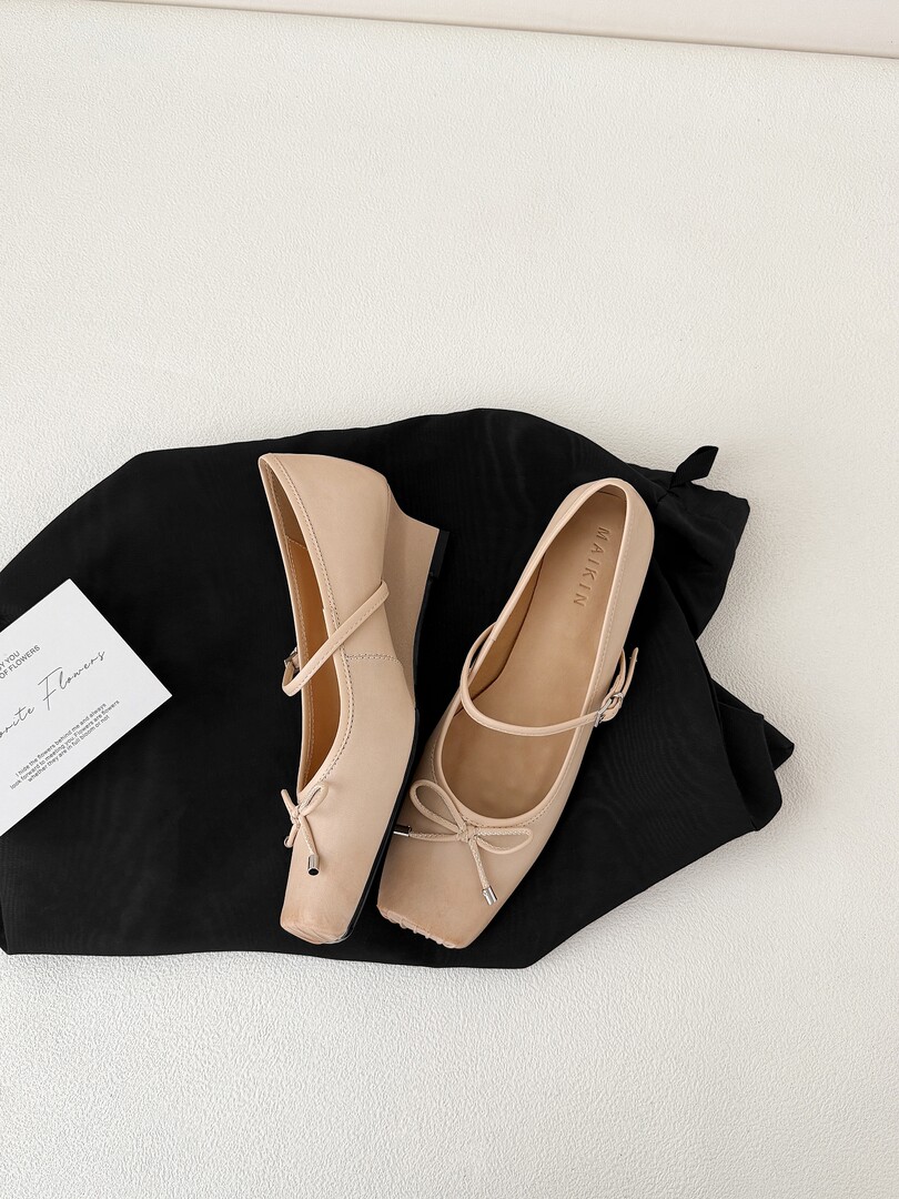 Beige pointed-toe flats with bow detail displayed on black fabric