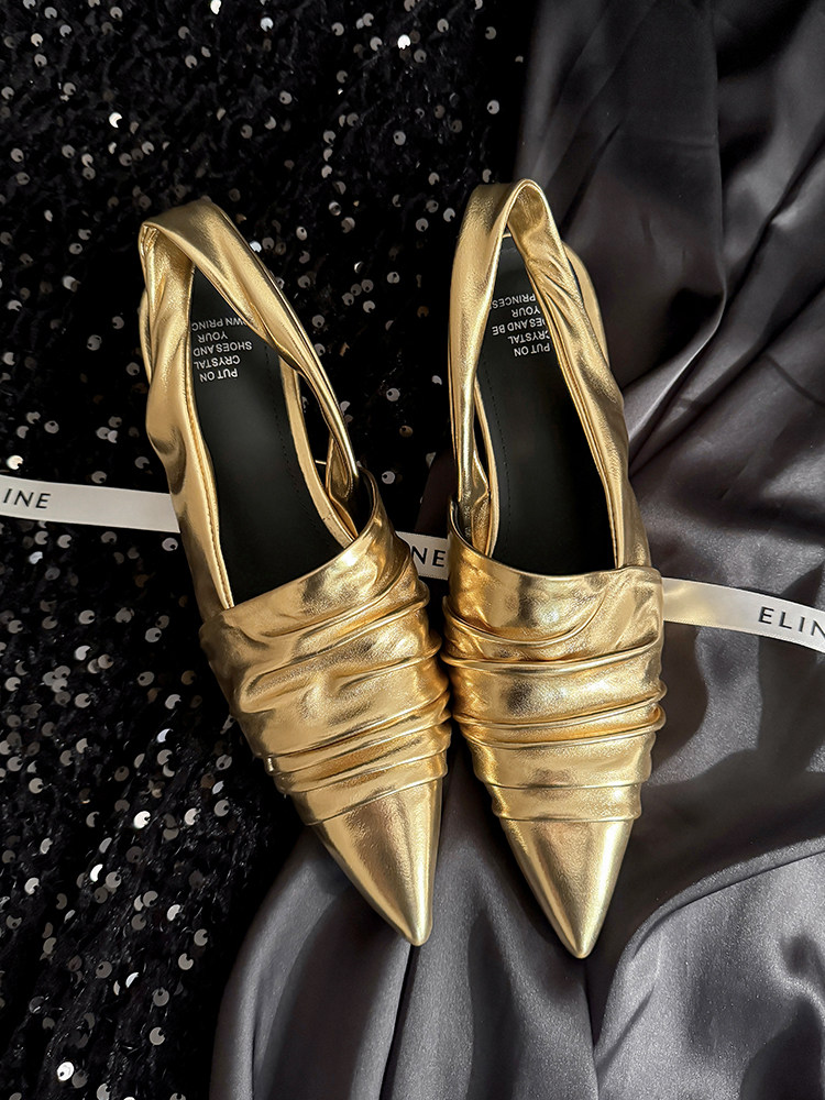 Pair of metallic gold pointed-toe flats laid on dark fabric